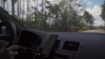 View from inside car on dashboard with smartphone. Mobile phone with gps navigation fixed in mounting. App map for travel. CMan use GPS navigation in phone with online map on screen while driving car. video