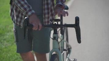 A cyclist walking near his bicycle is chatting online in the park in sunny weather. A commuter with a bicycle and a smartphone walking around. Man enjoys the phone on a summer walk with a bicycle. video