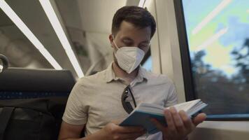Passenger on public transport is reading a book while sitting by window wearing a protective mask. A man traveling on a Deutsche Trains wearing a protective mask and reading a book. German railroad. video