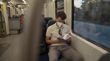 Passenger on public transport is reading a book while sitting by window wearing a protective mask. A man traveling on a Deutsche Trains wearing a protective mask and reading a book. German railroad. video