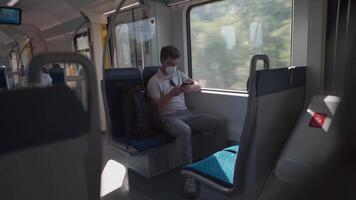 Passenger travelling by train wearing mask, using his phone to browse Internet. Masked man with smartphone on local railway car in Germany. Traveler on railroad with an alergic and air-pollution mask. video