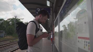 Thoughtful traveler using tourist transport map, looking for best way, transport connection standing at station in Germany, Munich. Man looking for location on mobile phone app and map board at stop video