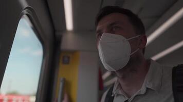A sad, tired man in a mask traveling on a railroad train, standing at the door and looking out the window. German National Railway. Masked male passenger standing at the doors of a suburban train. video