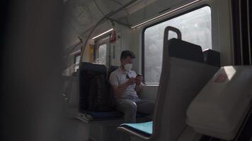 Passenger travelling by train wearing mask, using his phone to browse Internet. Masked man with smartphone on local railway car in Germany. Traveler on railroad with an alergic and air-pollution mask. video
