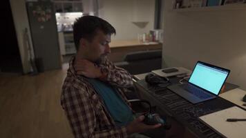 Cervical neck ache, nerve arthritis. Man studying late through night at laptop computer with cervical pain. Exhausted guy relaxing his neck using gun massager while overworking at notebook computer. video