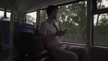 Man sits on bus wearing protective mask ffp2 uses smartphone in Germany, Munich. Passenger in protective mask in public transport and surfing Internet. Coronovirus rules of personal protection video