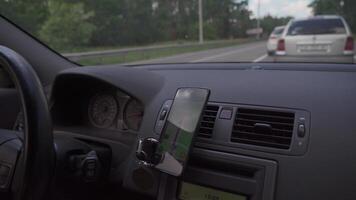 View from inside car on dashboard with smartphone. Mobile phone with gps navigation fixed in mounting. App map for travel. CMan use GPS navigation in phone with online map on screen while driving car. video