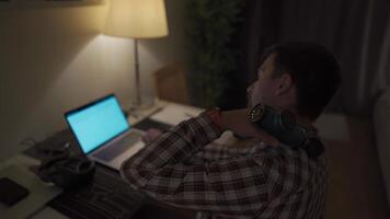 cervical nacke värk, nerv artrit. man studerar sent genom natt på bärbar dator dator med cervical smärta. utmattad kille avkopplande hans nacke använder sig av pistol massager medan överansträngning på anteckningsbok dator. video