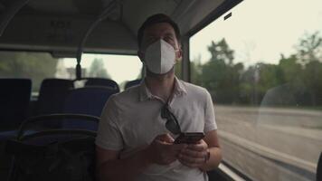 Passenger in ffp2 mask is on bus in Munich, browsing the Internet on mobile phone. Coronovirus regulations in Germany. Personal hygiene. Man on public transport using mobile app. Travel safely video