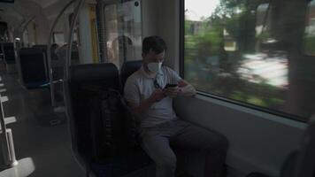 Passenger travelling by train wearing mask, using his phone to browse Internet. Masked man with smartphone on local railway car in Germany. Traveler on railroad with an alergic and air-pollution mask. video