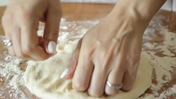 The hands of a female chef preparing a pizza dough base on a wooden table sprinkled with flour in close-up video