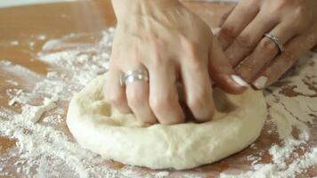 Knead the dough before baking. Hands roll out the dough on a wooden table sprinkled with wheat flour. video