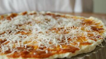 Making pizza. Dough with sauce and sprinkled with cheese. The cheese falls on the base of the pizza. video