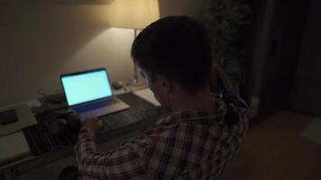 Cervical neck ache, nerve arthritis. Man studying late through night at laptop computer with cervical pain. Exhausted guy relaxing his neck using gun massager while overworking at notebook computer. video