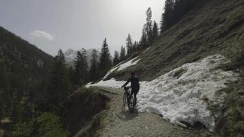 Man cyclist pulls bicycle through avalanche in mountains. Bicyclist is trapped in obstacle and is pulling his cycle through an ice slide with bicycle in his hands. Avalanche on cycling route in Alps. video