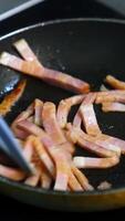 Chef cooking breakfast. Turning an amazing crispy bacon, rich in fat and colour. Sizzling and smoking in a hot pan. Vertical video