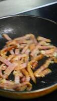 Frying bacon pieces in a pan. Crispy pieces of delicious bacon are fried in a hot skillet. Unhealthy food. Vertical video