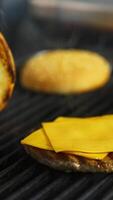 Hands of a person fry buns on grill. Meat cutlet with cheese on top. Fast food concept. Vertical video