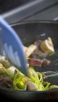 Mushrooms fried with vegetablesin a big frying pan. Chef turns fried ingredients with spatula. Vertical video