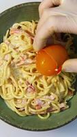 Spaghetti carbonara. Carbonara is made with eggs, bacon, pepper and grated pecorino cheese. Chef puts egg yolk to the dish. Vertical video