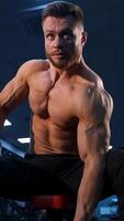Handsome strong young bodybuilder work out with dumbbells. Strong abs. Modern gym background. from below. Vertical video