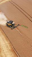 New yellow harvesting machine in the abundant farmland. Agricultural machine declined from a straight way and went diagonally in the field. Top view. Vertical video