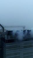 High metal constructions, supports and pipes at the modern elevator plant. Thick white smoke coming into camera. Grey foggy day backdrop. Vertical video