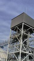 High metal construction standing next to the elevator tanks. Looking at the tops of modern granary buildings at the backdrop of grey cloudy sky. Vertical video