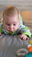 Tiny boy lies on the bed and toy is in front of him. Cute kid moving arms and legs actively, making funny faces. Grey backdrop in blur. Vertical video