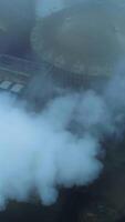 Huge functioning agribusiness plant for grain storage and processing. Top view on the silo tanks roofs in the white smoke and fog. Vertical video