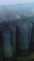 Gloomy sight of an agricultural granary plant. View from above on the modern elevator for grain storage. Foggy winter weather background. Vertical video