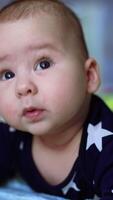 Nice adorable little kid looks up lying on belly. Cute child gazing dreamily and with curiosity up. Close up. Blurred backdrop. Vertical video