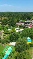 Sunlit green territory of beautiful spa resort in the countryside. Swimming-pool with people resting around it. Aerial perspective. Vertical video
