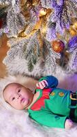 Caucasian child in green elf costume and red socks with deer resting on the fluffy plaid. Beautiful toddler moving legs actively under Christmas tree. Vertical video