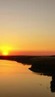 Orange sunset. Beautiful view of river under colorful sky of the setting sun. Amazing sunset on water surface. Aerial view. Vertical video