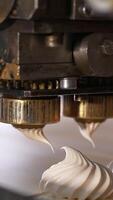 Few metal nozzles rotate and squeeze creamy marshmallows on conveyor belt. Automated line for desserts manufacturing. Close up. Vertical video