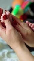 Caring and loving mother's hands caressing bare feet of her son. Newborn kid is busy with a toy while mum is rubbing tiny baby toes. Vertical video