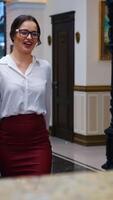 Charming lady with suitcase in the reception lobby. Girl approaching hotel reception to take the key. Portrait of gorgeous woman pressing bell button at reception desk. Vertical video