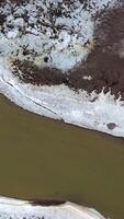Muddy water. Flight over the dirty narrow river floating among polluted field in springtime. Ecological disaster. Aerial view. Vertical video