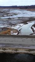 Gloomy scene of nature. Polluted river floating under the bridge on muddy background in springtime. Ecological problems. View from above. Vertical video