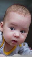 Toddler boy stays up and tries to hold his head up. Cute little kid looking around. Close up. Blurred backdrop. Vertical video
