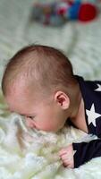 Little boy lying on his belly on the bed learning how to hold up head. Beautiful child looks quite surprised into camera. White backdrop in blur. Vertical video
