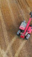 Modern red skid steer loader moving quickly by the field and picking straw. Tiny agile machine gathering hay bales in the farmlands. Top view. Vertical video