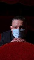 Spectator in medical mask sitting alone in theater. One man in protective mask watching a play in empty auditorium during coronavirus. Vertical video