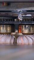 Rotating metal nozzles lay creamy substance on the conveyor belt to create beautifully-shaped marshmallows. Close up. Food factory concept. Vertical video