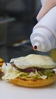 Making hamburger in fast food restaurant. Hand of man smears sauce on a burger and covers with fried bread. Close-up.Tasty burgery ready to eat. Vertical video