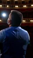 Actor on stage. Man in medical mask is talking to empty auditorium. Speaker in protective mask during the rehearsal. Rear view. Vertical video