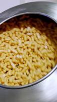 Metal tank rotating and mixing the corn snacks inside. Thick maize sticks are covered with sugar glazing. Food factory production. Vertical video