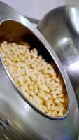 Rotating metal tank full of yellow corn sticks. Other tank is filled with corn snacks from a metal nozzle at backdrop. Vertical video