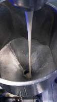 Condensed milk streaming from a tube into a metal container. Close up. Food factory automated line. View from above. Vertical video